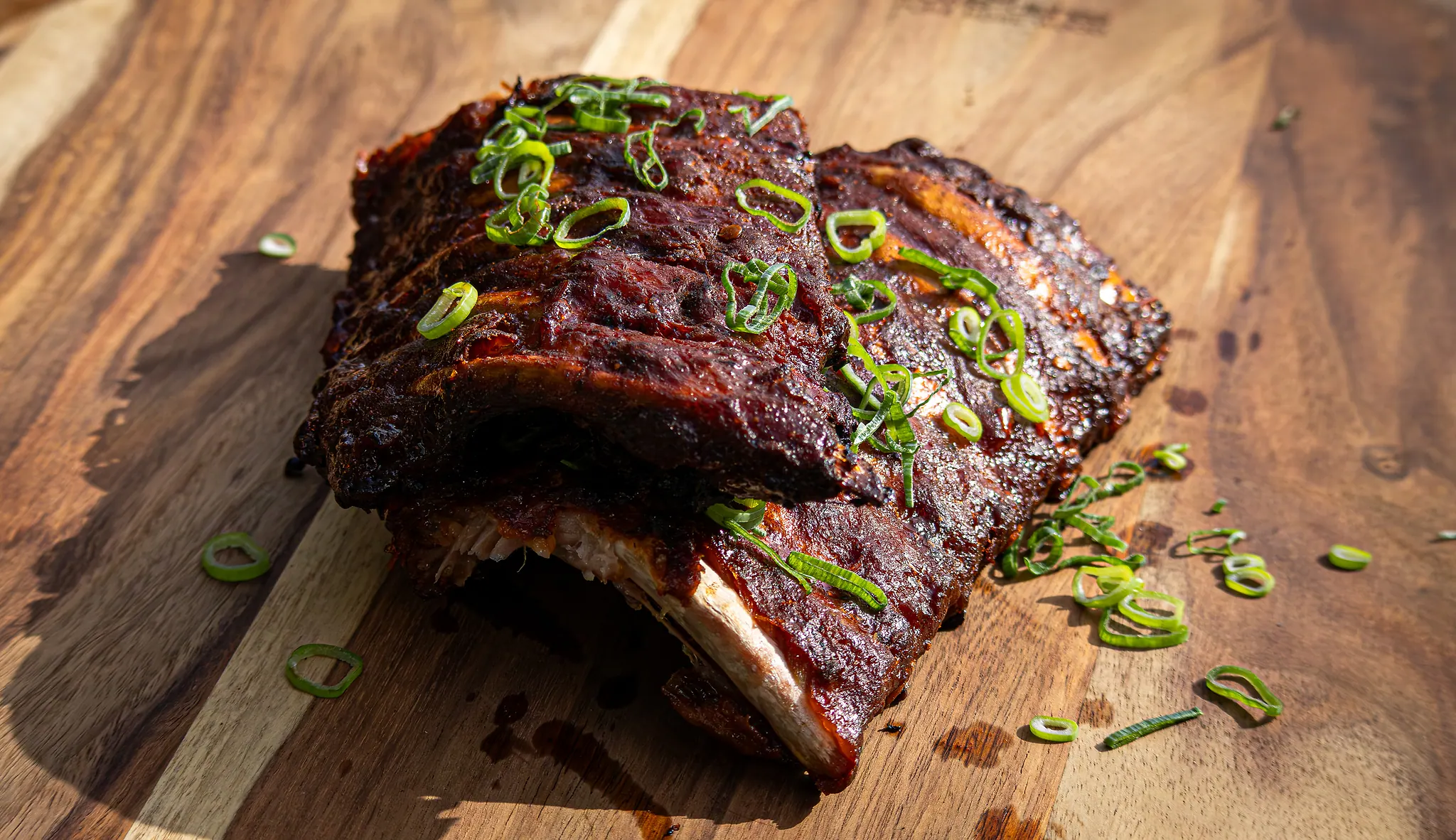 Ribs uit de rook, gesneden op een houten plank, met lente-ui.