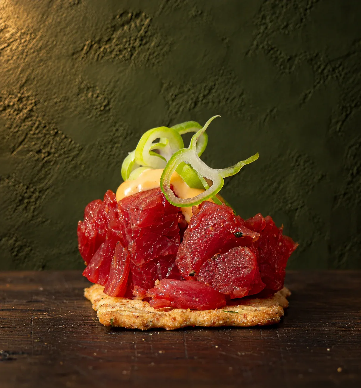 Tartaar op een cracker, met een toef saus en krullen lente-ui.