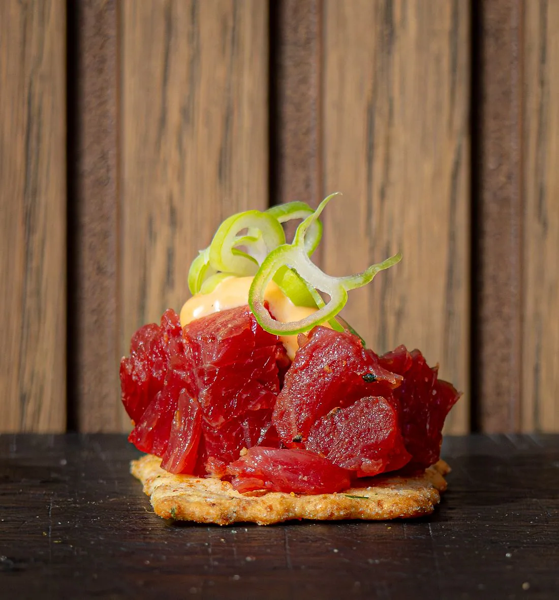 Gepekelde bavette op een cracker, met een krul lente-ui.
