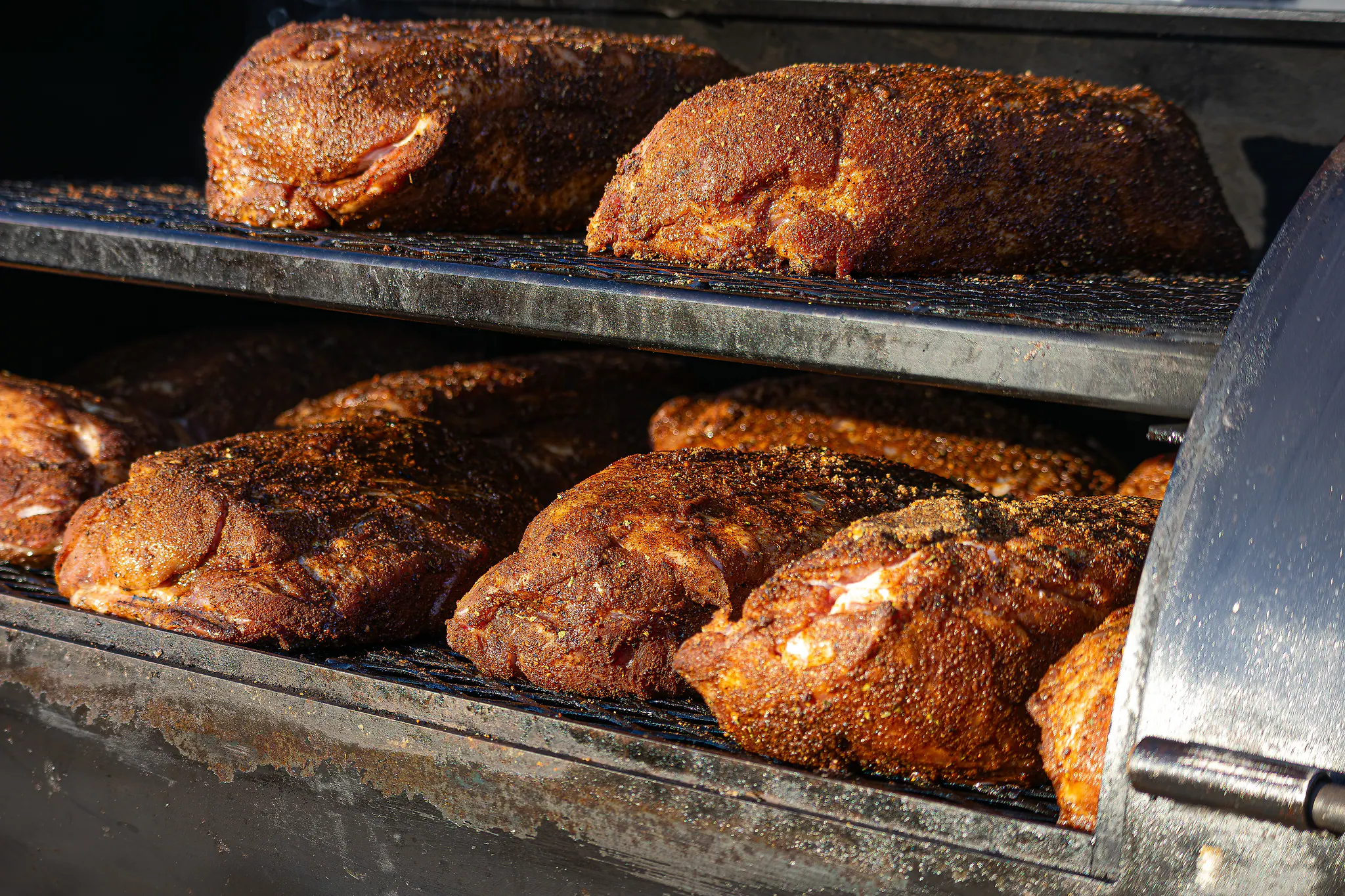 Grote stukken vlees met rub op de roosters in de smoker.